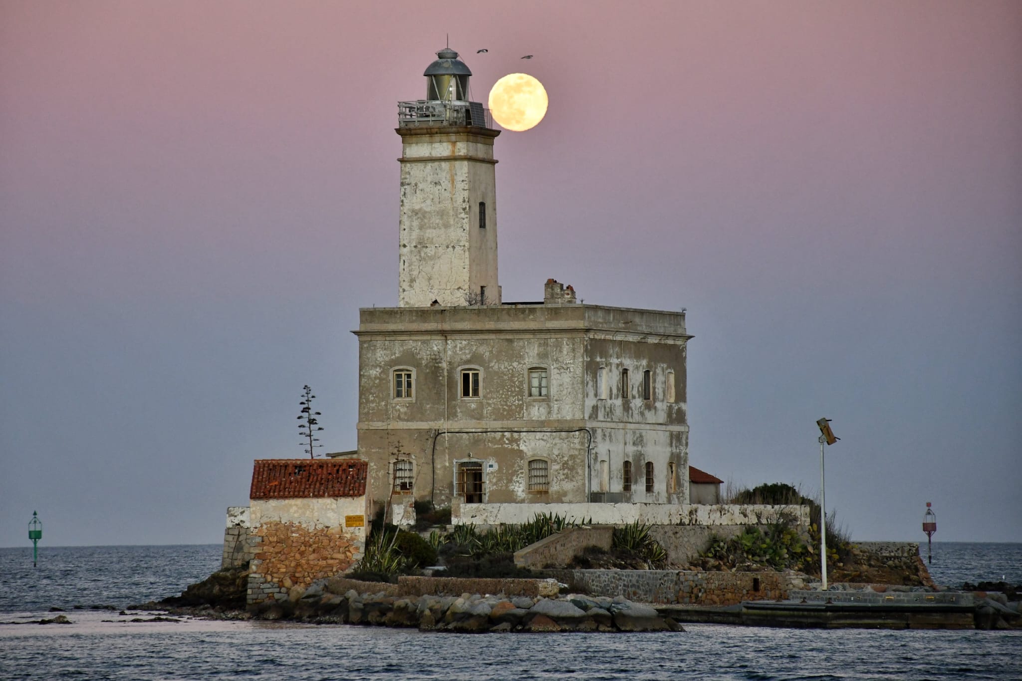 Olbia, l'ultima luna piena fa capolino sul faro del Lido del Sole